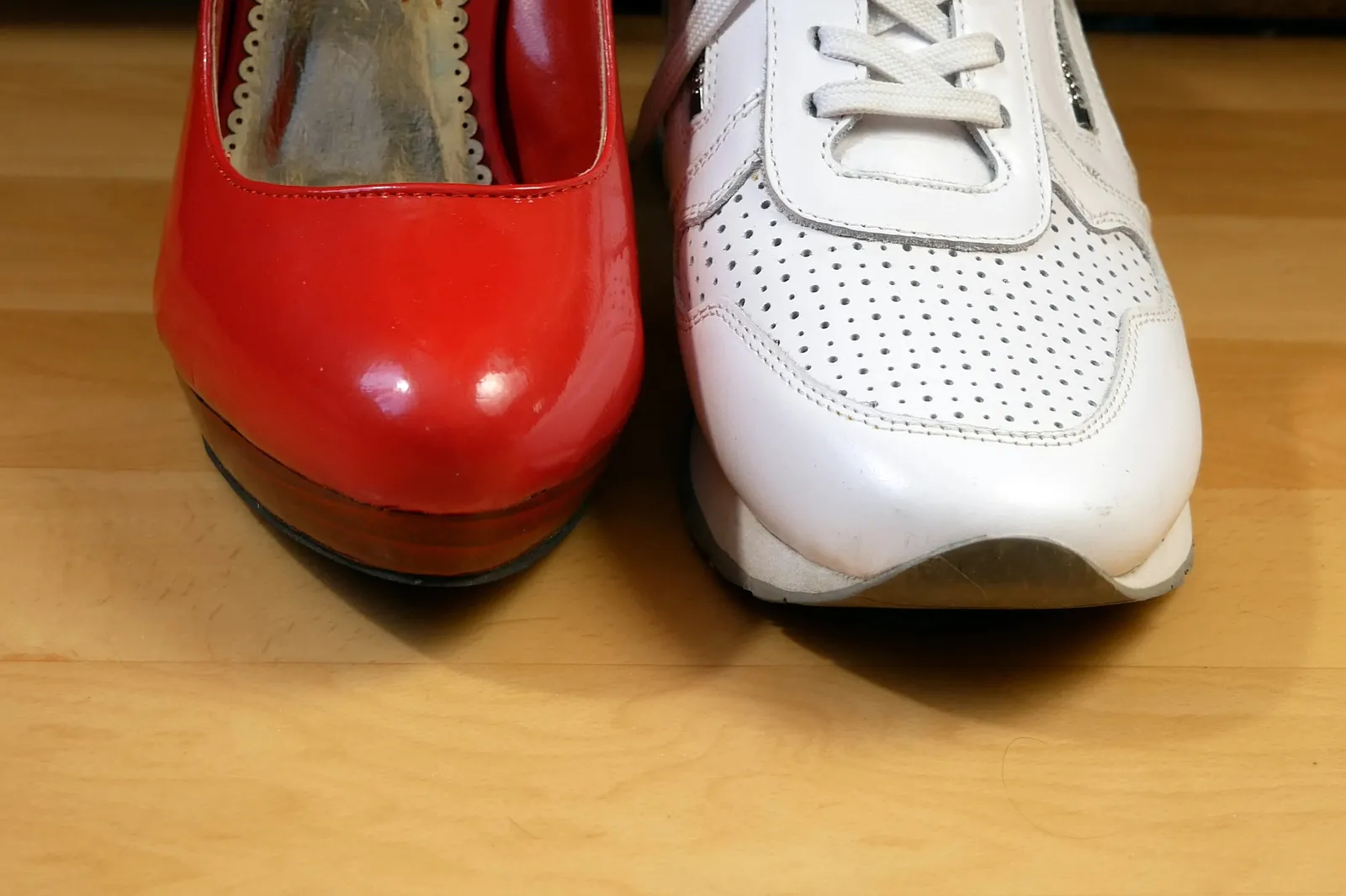 Zapato rojo de tacón en un pie y zapatilla blanca de suela plana en el otro