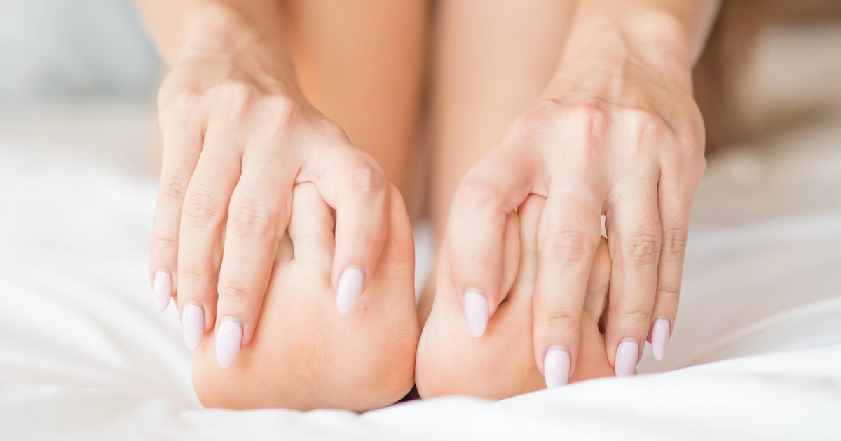 Manos sujetando los dedos de los pies por molestias en la articulación del dedo gordo