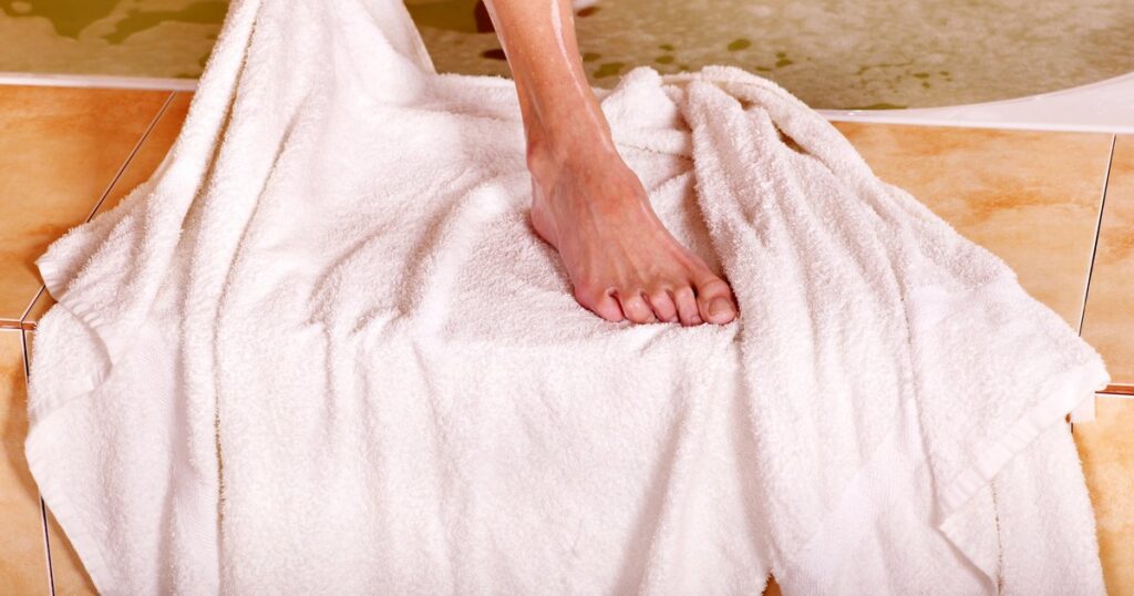 Mujer secándose los pies con una toalla blanca al salir del baño
